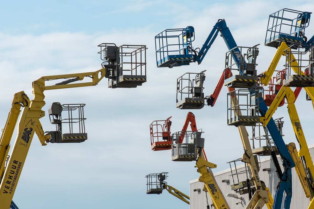 A collection of colorful boom lifts reaching toward a clear blue sky, showcasing industrial machinery.